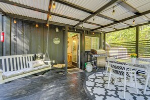 A covered outdoor seating area with a swing chair, a table with chairs, and a patterned rug. - Blue Ridge Mountain Tiny Home: Escape to Nature! (Old Fort)