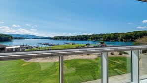A view from a balcony overlooking a lake with a dock, grassy areas, and distant hills. - Beach + Pool Access: Smith Mountain Lake Getaway! (Huddleston)