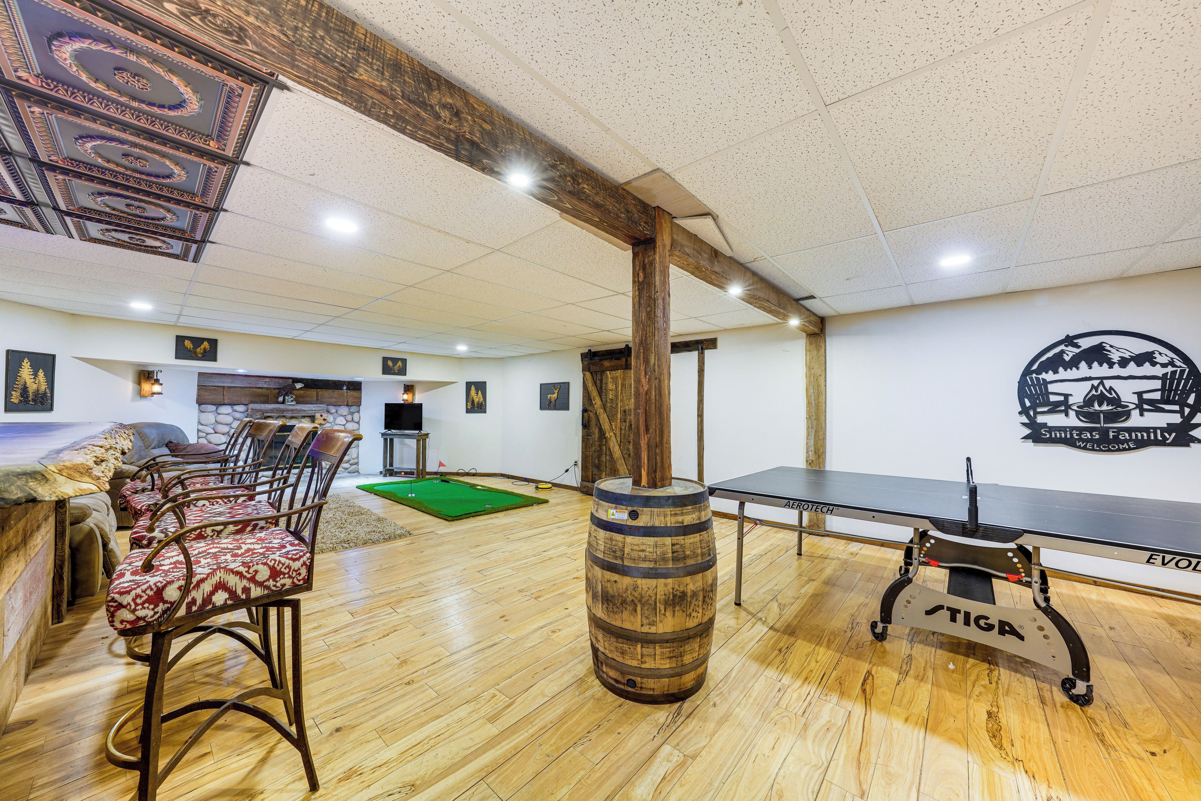 Une pièce avec un plancher en bois, un tabouret de bar, un tonneau en bois, une table de ping-pong et un mur orné d’un logo.