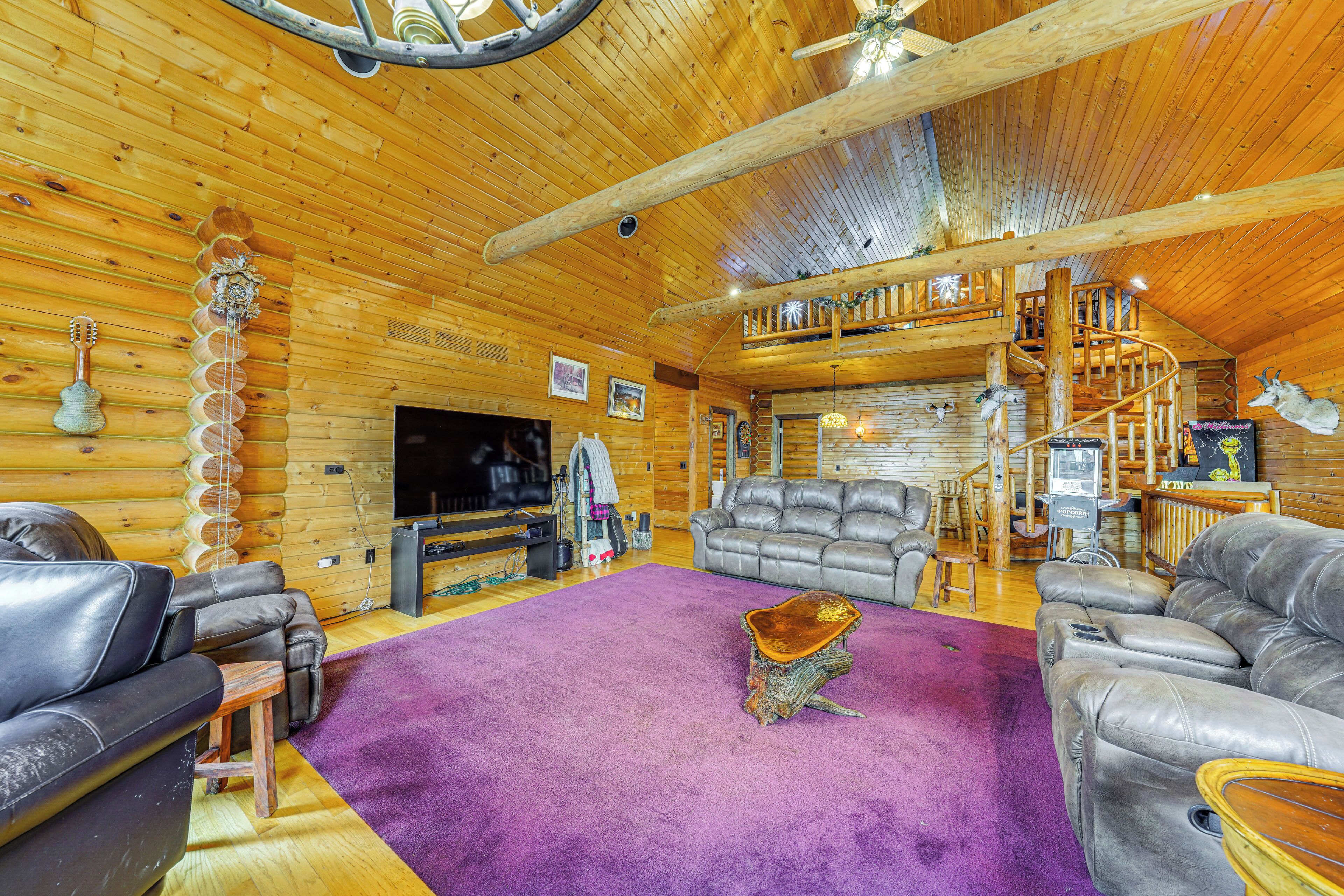 A log cabin interior with a wooden ceiling, a large TV, leather sofas, and a purple carpet.