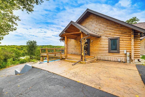 A log cabin with a porch, a welcome sign, and a view of the surrounding greenery.