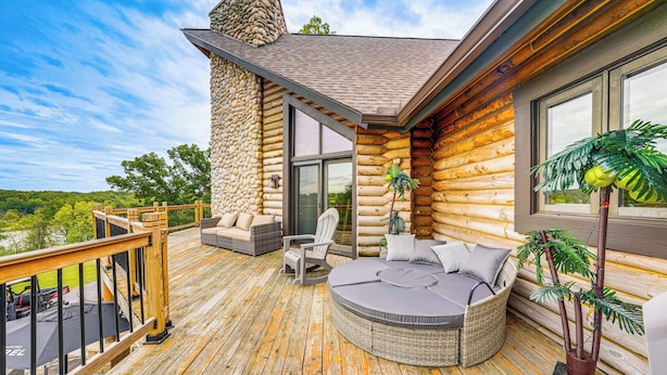 Eine Blockhütte mit einer Terrasse, Sitzgelegenheiten im Freien und einem großen Fenster.