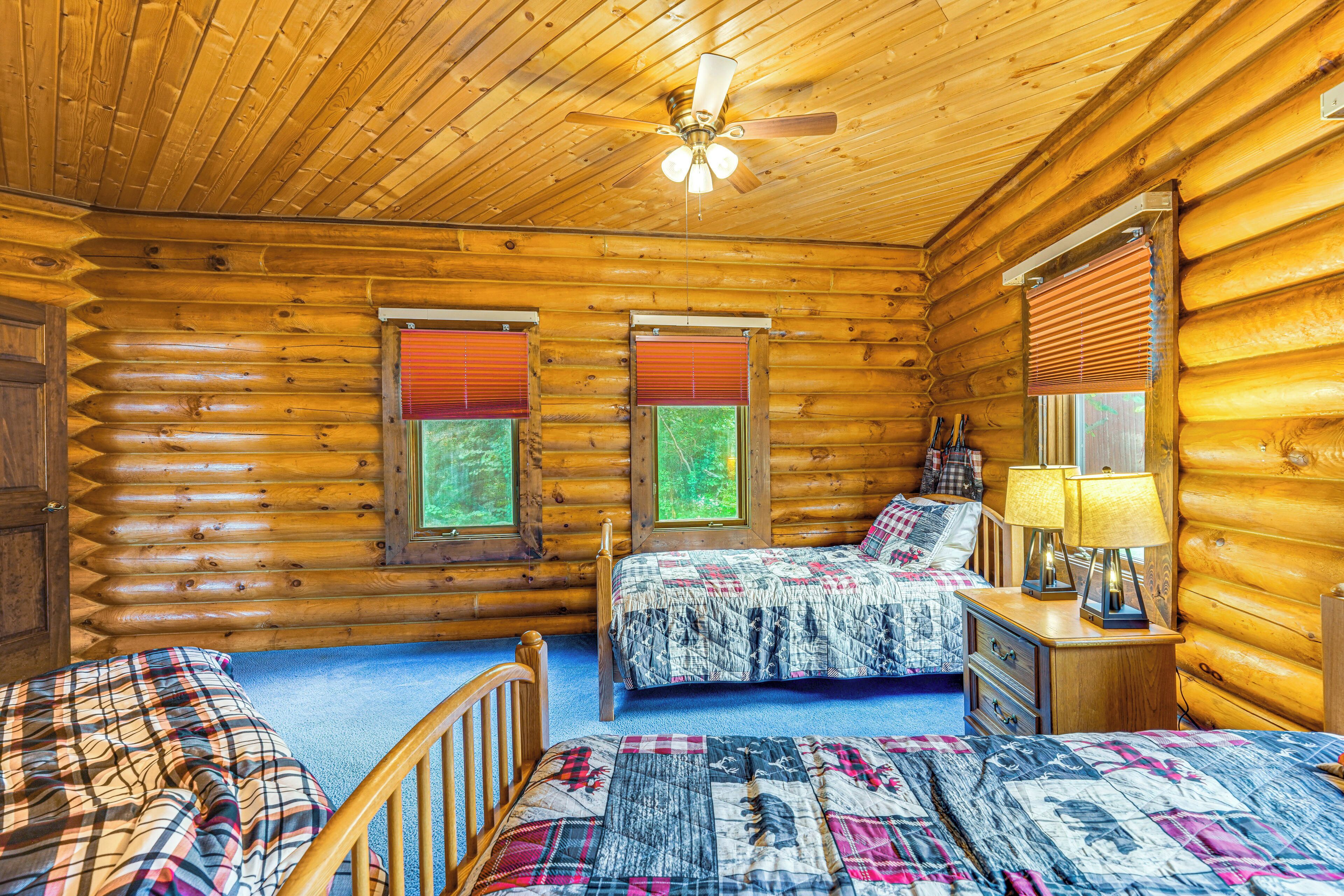 A log cabin bedroom with two beds, a ceiling fan, and wooden walls.