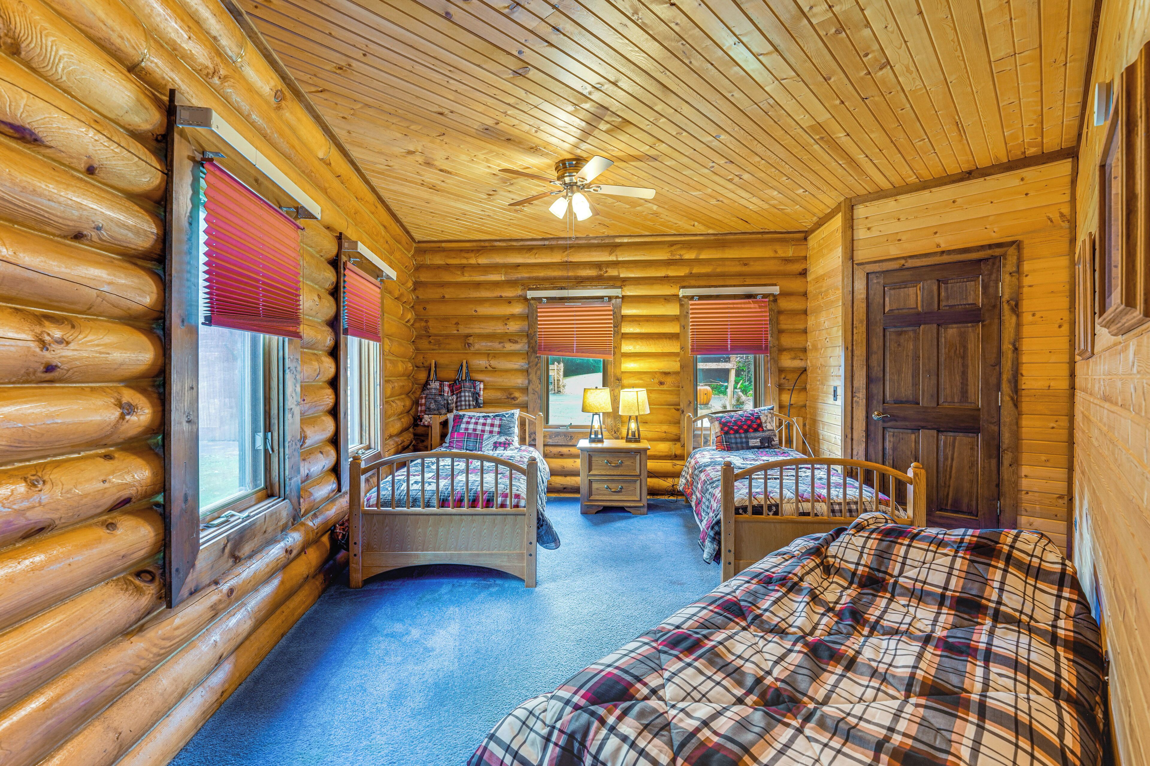 A log cabin bedroom with two beds, a ceiling fan, and a wooden door.