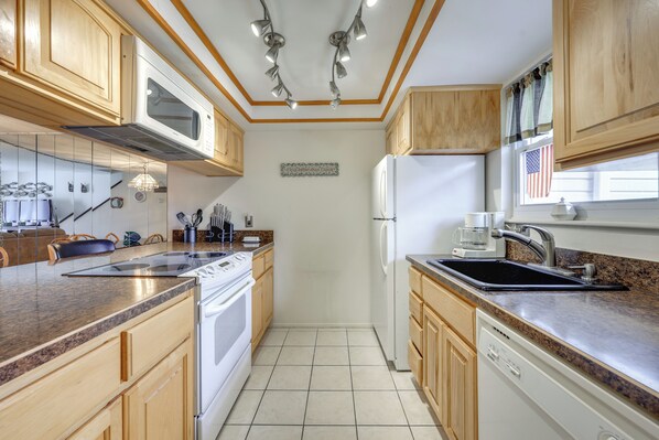 A kitchen with wooden cabinets, a microwave, stove, refrigerator, and a sink. - Riverfront Weleka Condo w/ Dock & Pool Access (Welaka)