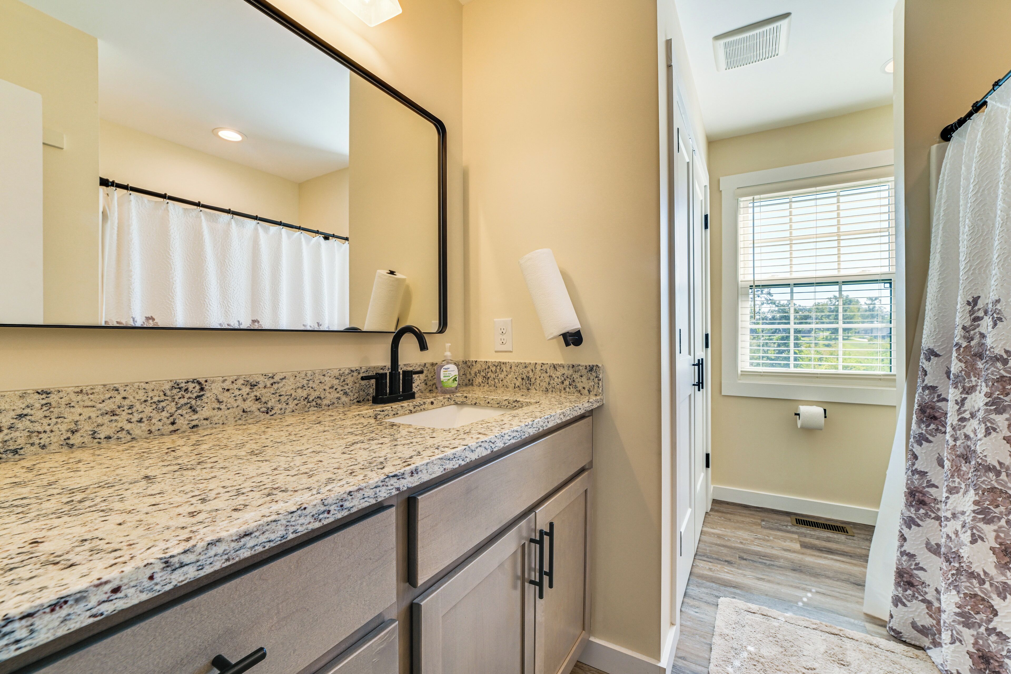 A bathroom with a granite countertop, a sink, a mirror, and a shower curtain.