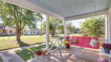 Eine überdachte Veranda mit Holzboden, einer roten Bank mit Kissen und Blumentöpfen.
