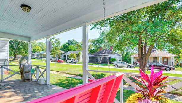 A covered porch with a red bench, a flower arrangement, and a view of a residential street. - 3 Mi to Downtown Covington: Cozy Getaway w/ Porch! (Porterdale)