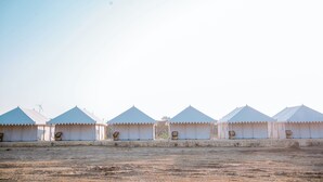 Une rangée de tentes blanches, au design simple et fonctionnel, disposées en ligne sur un terrain plat et désolé.