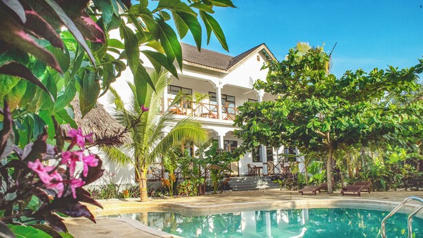 A pool area with a stone deck, surrounded by lush greenery and a white building with multiple balconies. - Yasa Boutique Hotel (Nungwi)