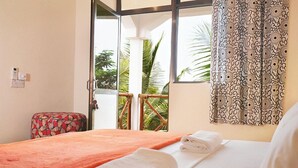 A hotel room with a bed, a small table, a chair, and a balcony with a view of palm trees. - Yasa Boutique Hotel (Nungwi)