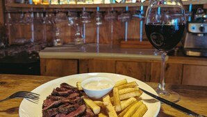 A plate of steak and fries with a glass of red wine on a wooden table. - Yasa Boutique Hotel (Nungwi)
