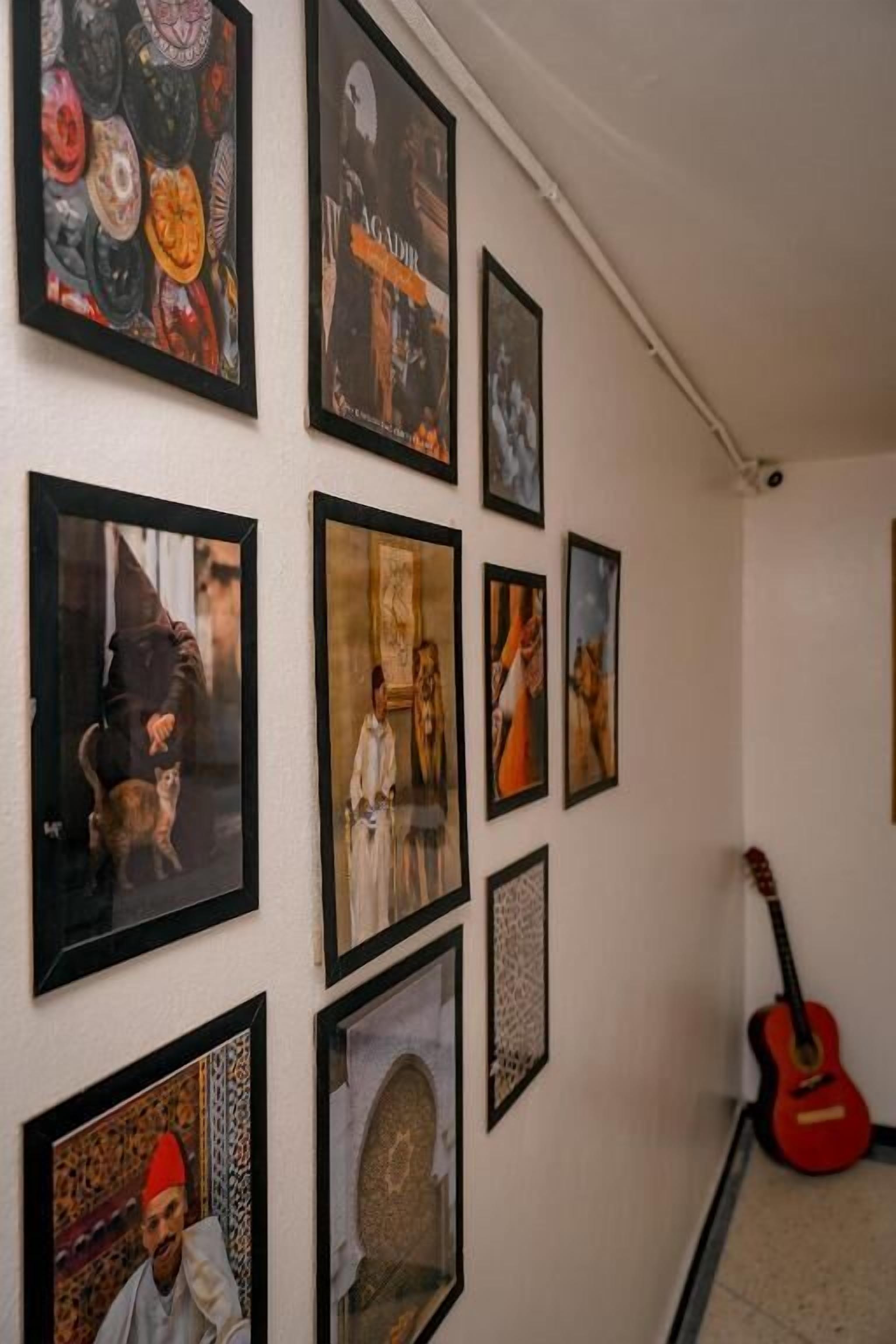 A hallway with framed artwork on the walls, a guitar leaning against the wall, and a tiled floor.