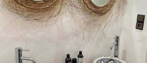 A bathroom with two round mirrors framed by woven materials, a wooden vanity with a decorative sink, and a small green soap dish.
