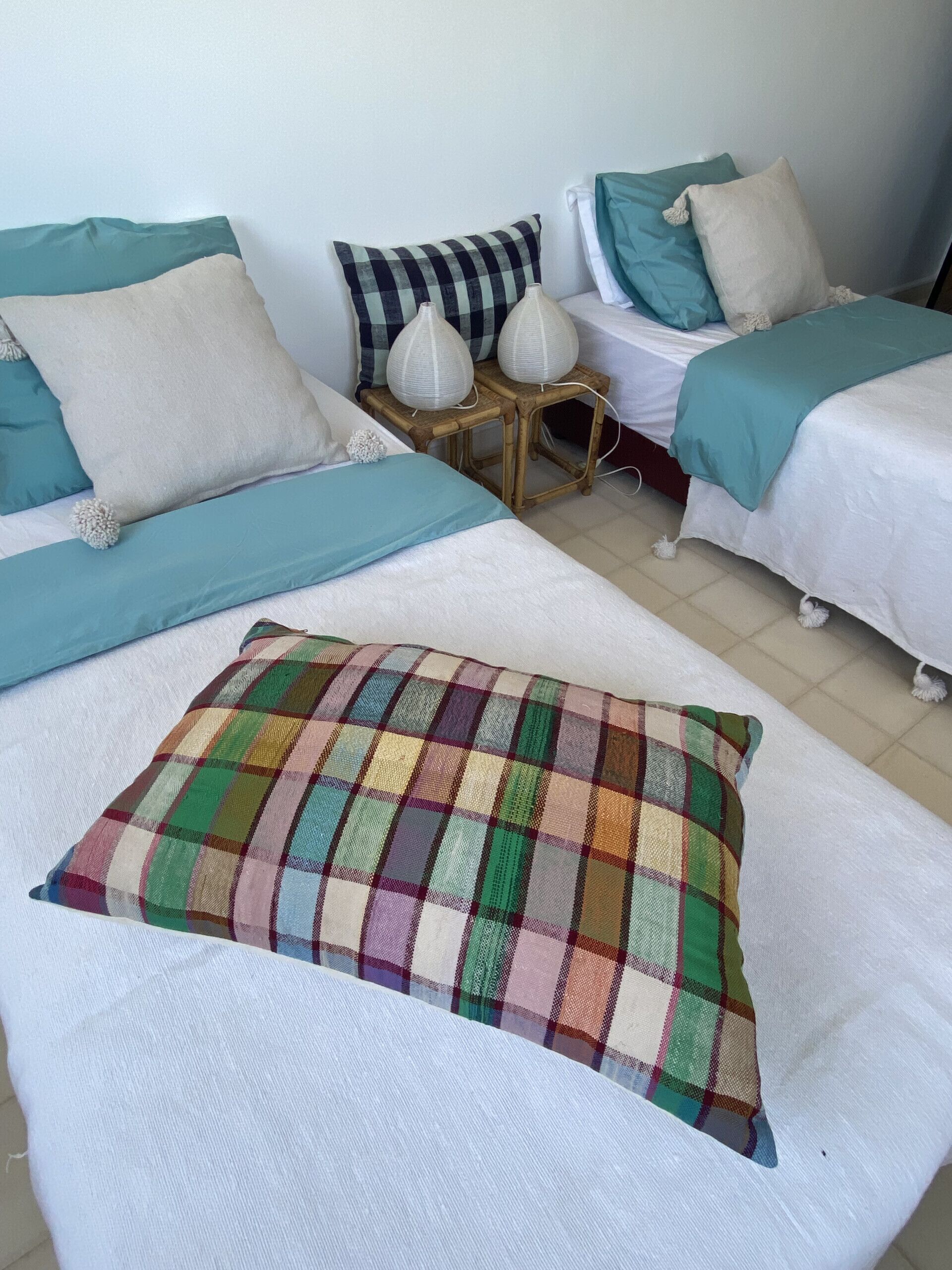 Quarto com duas camas, cada uma com colcha branca e várias almofadas. Há duas mesinhas com luminárias brancas entre as camas.