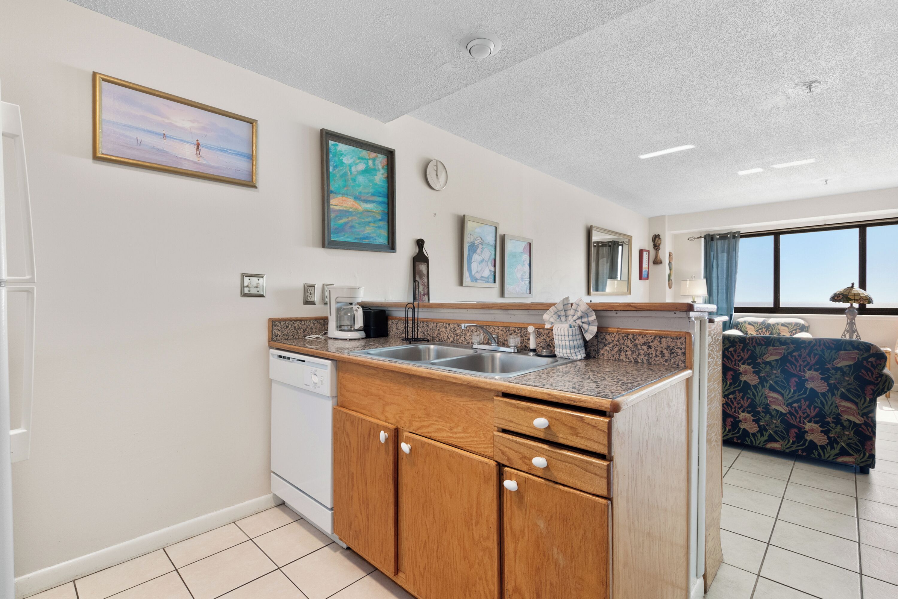 A modern kitchen with wooden cabinets, a built-in dishwasher, and a large window offering a view of the outdoors.