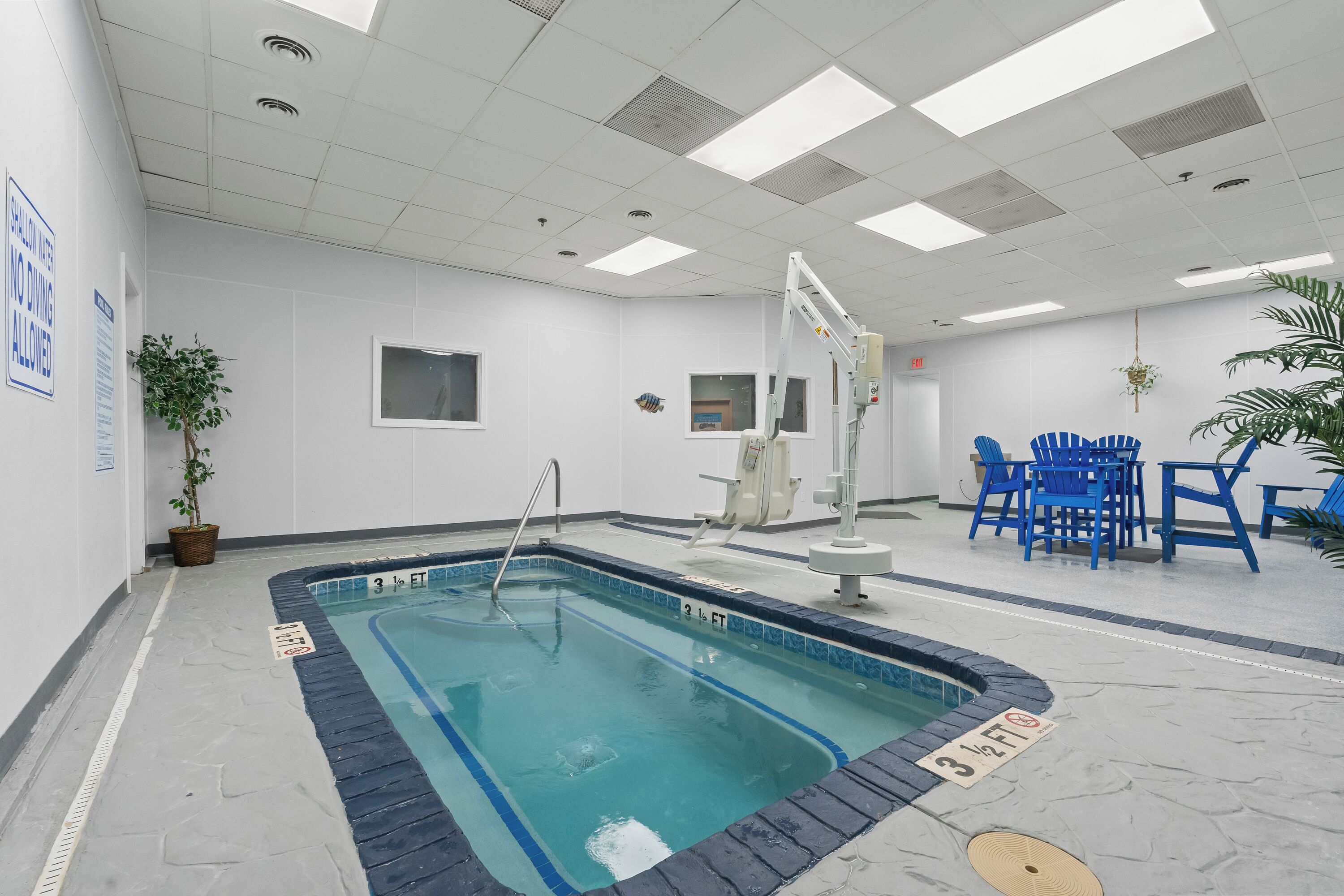 Una piscina con una silla de salvavidas, una silla azul y una ventana pequeña.