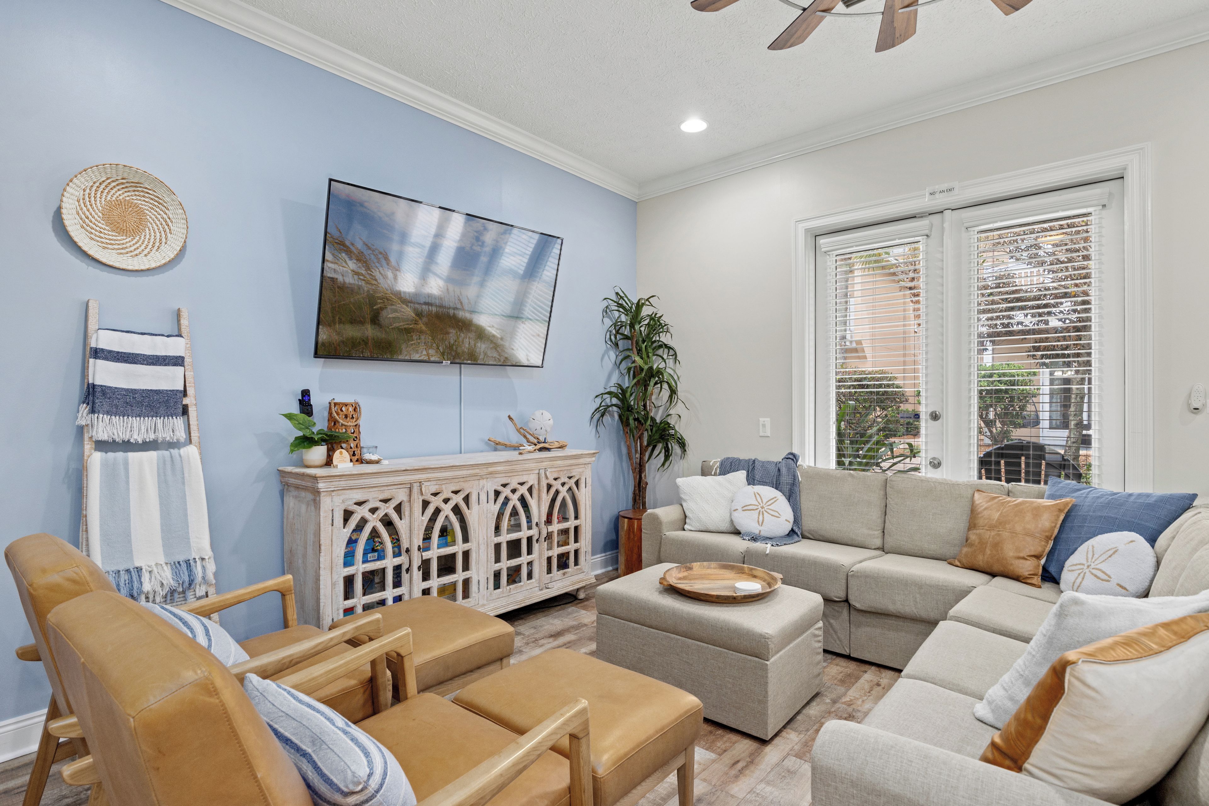 Un salon avec un mur bleu clair, un grand téléviseur à écran plat, un meuble en bois, un canapé beige et une chaise en bois.