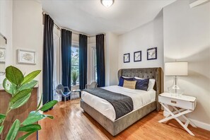 Een slaapkamer met een groot bed, een nachtkastje met een lamp, en uitzicht op de omgeving door het raam.