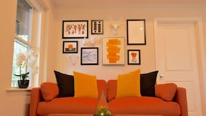 Una sala de estar con un sofá, una mesa de centro de vidrio y varias obras de arte enmarcadas en la pared.