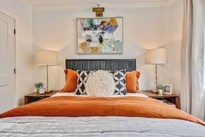 A neatly arranged bedroom with a large bed, two bedside tables, a wall-mounted lamp, and a framed artwork above the bed. - Mid-Century Glam Retreat, Near T (Boston)