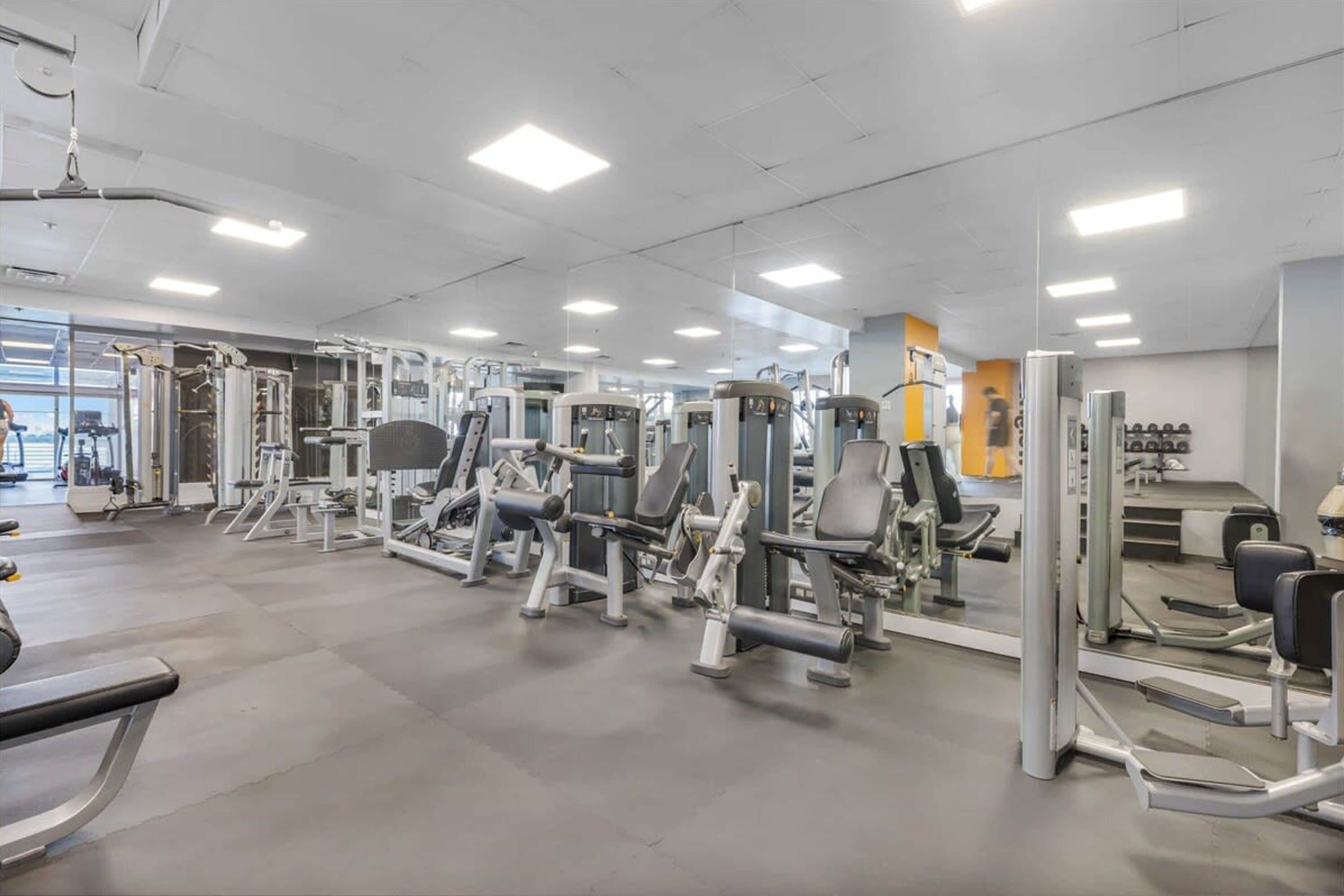 Un gimnasio con diversas máquinas de ejercicio, espejos y un ambiente limpio y bien iluminado.