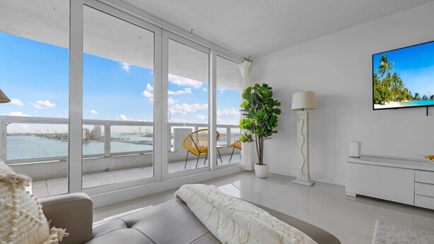 A modern living room with a large window, a sofa, a TV, and a plant. - The Grand Wonder Biscayne (Miami)