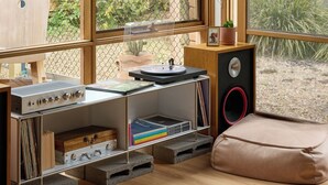 A room with a wooden ceiling, large windows, a wooden cabinet, a speaker, and a bean bag chair.