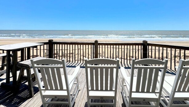 Una terraza de madera con sillas blancas que da a la playa.
