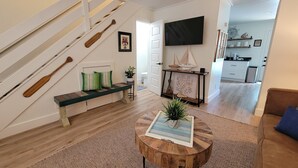 A modern living room with a wooden bench, a round wooden coffee table with a plant, a staircase with wooden paddles, and a kitchen in the background. - "Sweet Reward"-*Labor Day Special!* Location X3! Pet Friendly! (Gulf Shores)