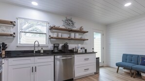 A modern kitchen with white cabinets, a stainless steel dishwasher, and wooden shelves above the counter. - "Sweet Reward"-*Labor Day Special!* Location X3! Pet Friendly! (Gulf Shores)
