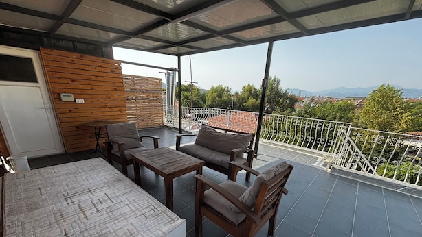 A balcony with a wooden table and chairs, a sofa, and a view of the cityscape.