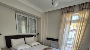 Une chambre bien rangée, avec un lit, des tables de chevet, une fenêtre avec des stores, un radiateur et une vue sur l’extérieur.
