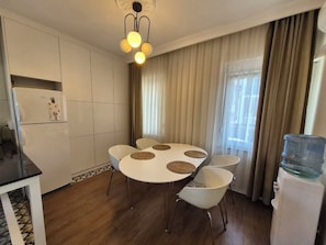 A compact kitchen with a round dining table, white chairs, a water dispenser, and a refrigerator. - Vacation apartment in the heart of Fethiye  (Fethiye)
