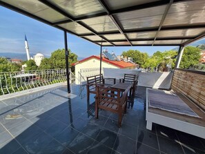 A rooftop terrace with a table and chairs, a covered seating area, and a view of a mosque and mountains. - Vacation apartment in the heart of Fethiye  (Fethiye)