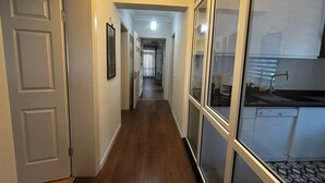A hallway with wooden flooring, white walls, and a door on the left.