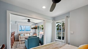 A bedroom with a bed, a ceiling fan, and a view of the outdoor balcony. - Kailani #213, Oceanfront, Sunrise and Moon Rise Views! (Kapaa)
