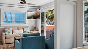 A modern living room with a sofa, two armchairs, a flat-screen TV, and a ceiling fan. - Kailani #213, Oceanfront, Sunrise and Moon Rise Views! (Kapaa)