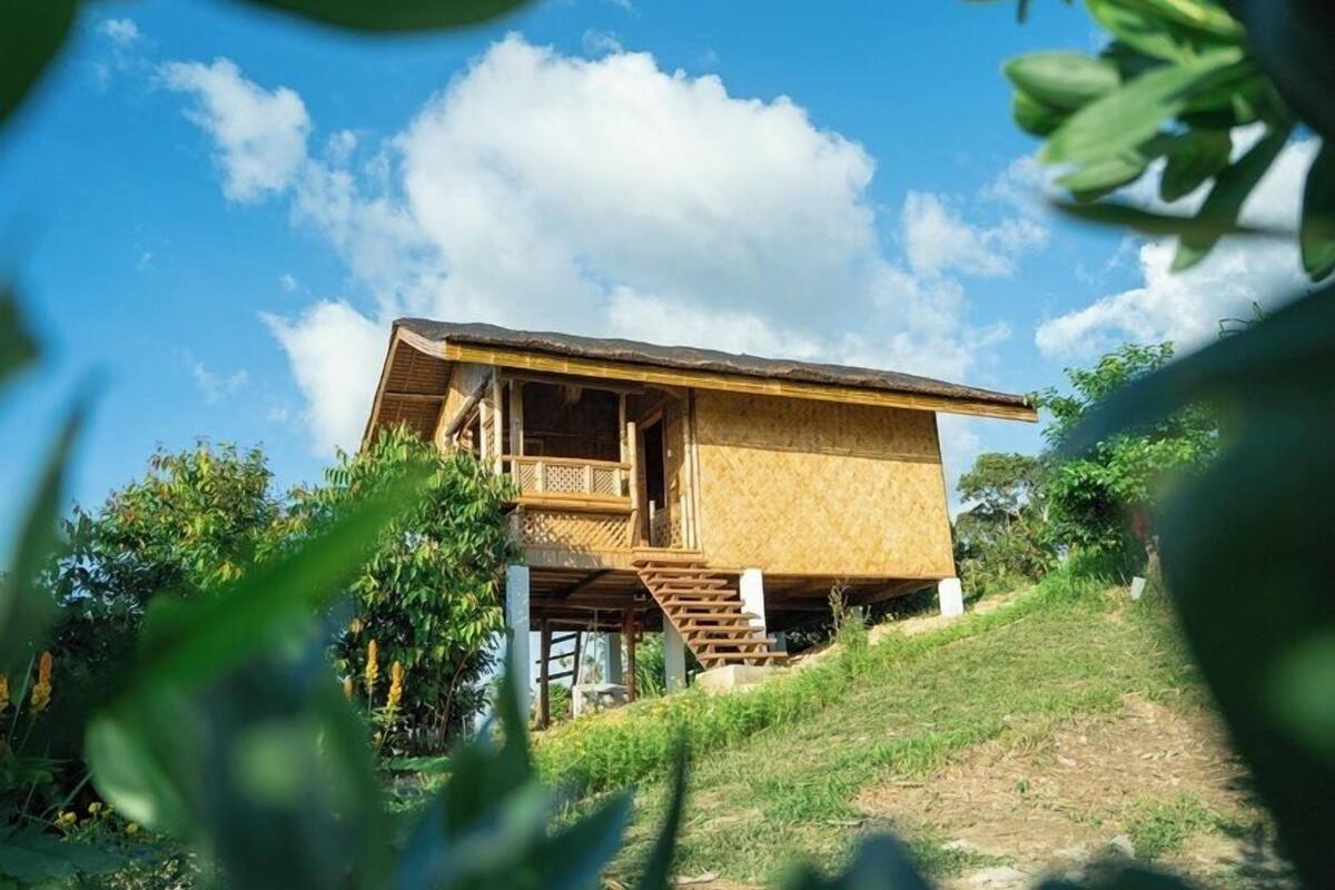 Una casa de madera con balcón, rodeada de follaje y un cielo despejado.