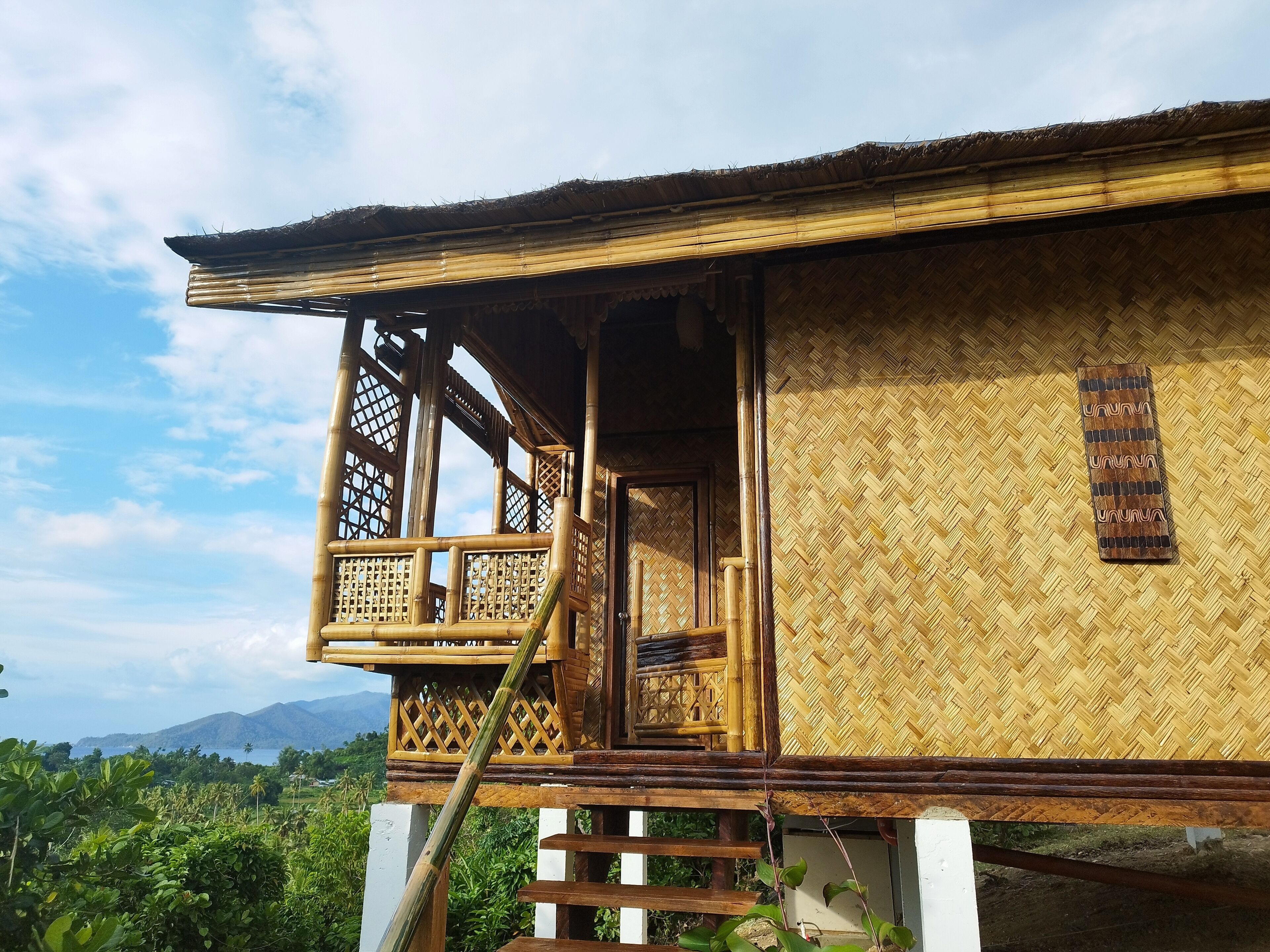 Una casa tradicional de bambú con balcón, una escalera y vistas del paisaje circundante.