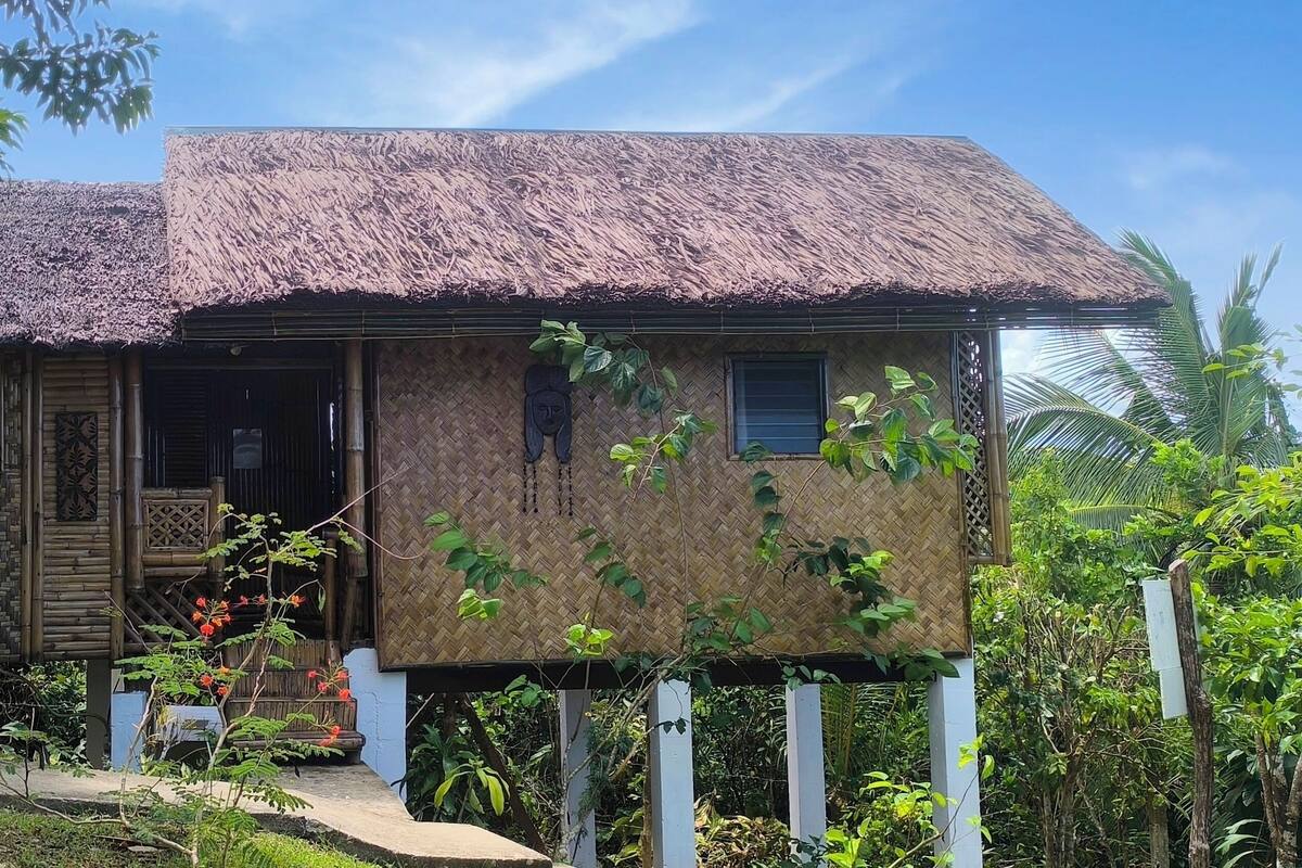 Una casa tradicional con techo de paja y fachada de madera, rodeada de abundante vegetación.
