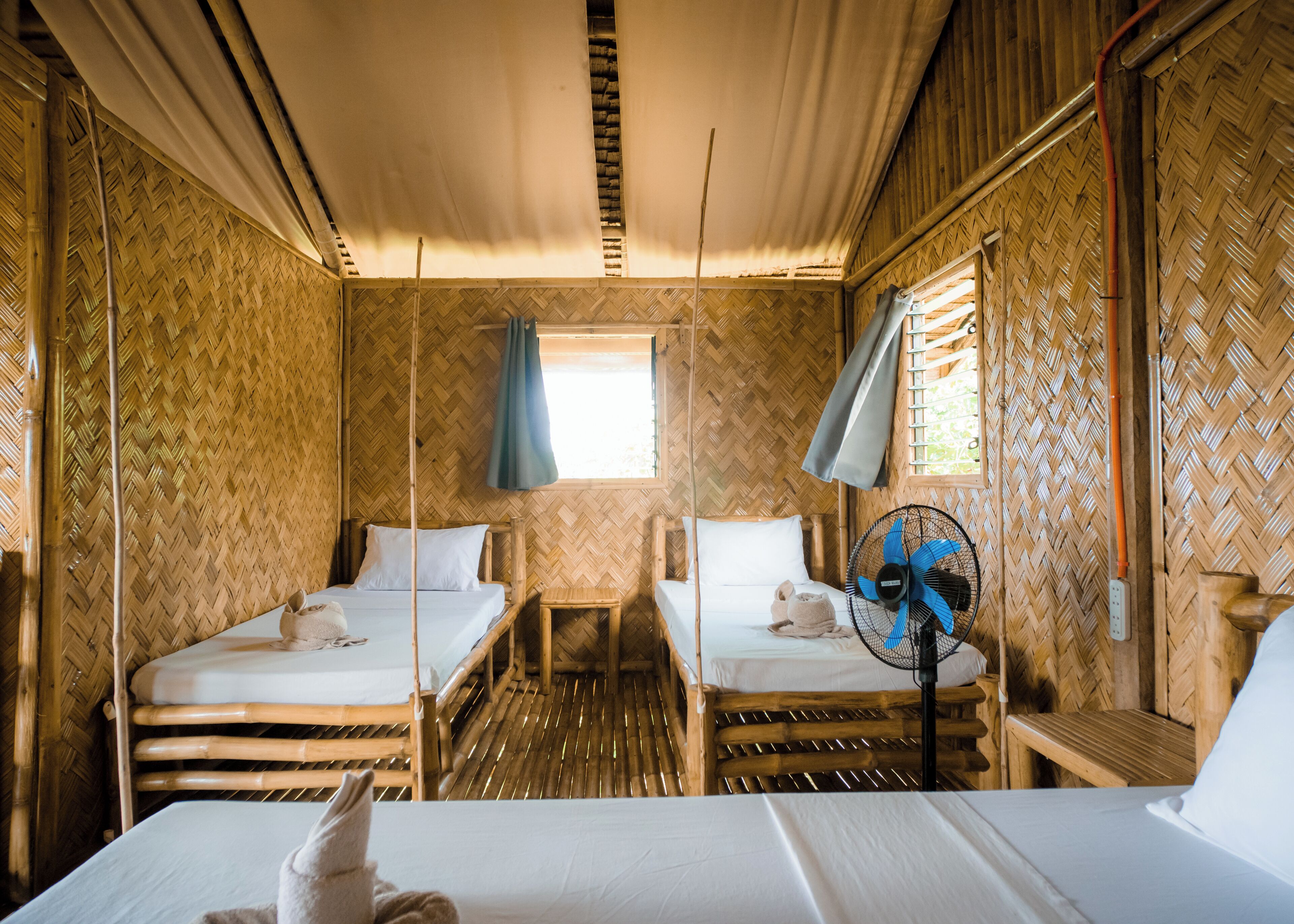 A room with two single beds, a small table, and a fan.
