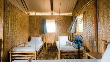 A room with two single beds, a small table, and a fan.