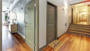 Un couloir d’hôtel avec un plancher en bois, un paillasson et un escalier menant à une sortie.