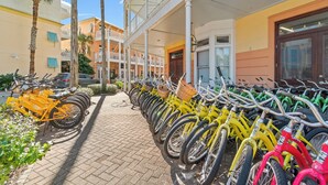 Een rij felgekleurde fietsen geparkeerd voor een gebouw met een balkon, en een auto op de achtergrond.