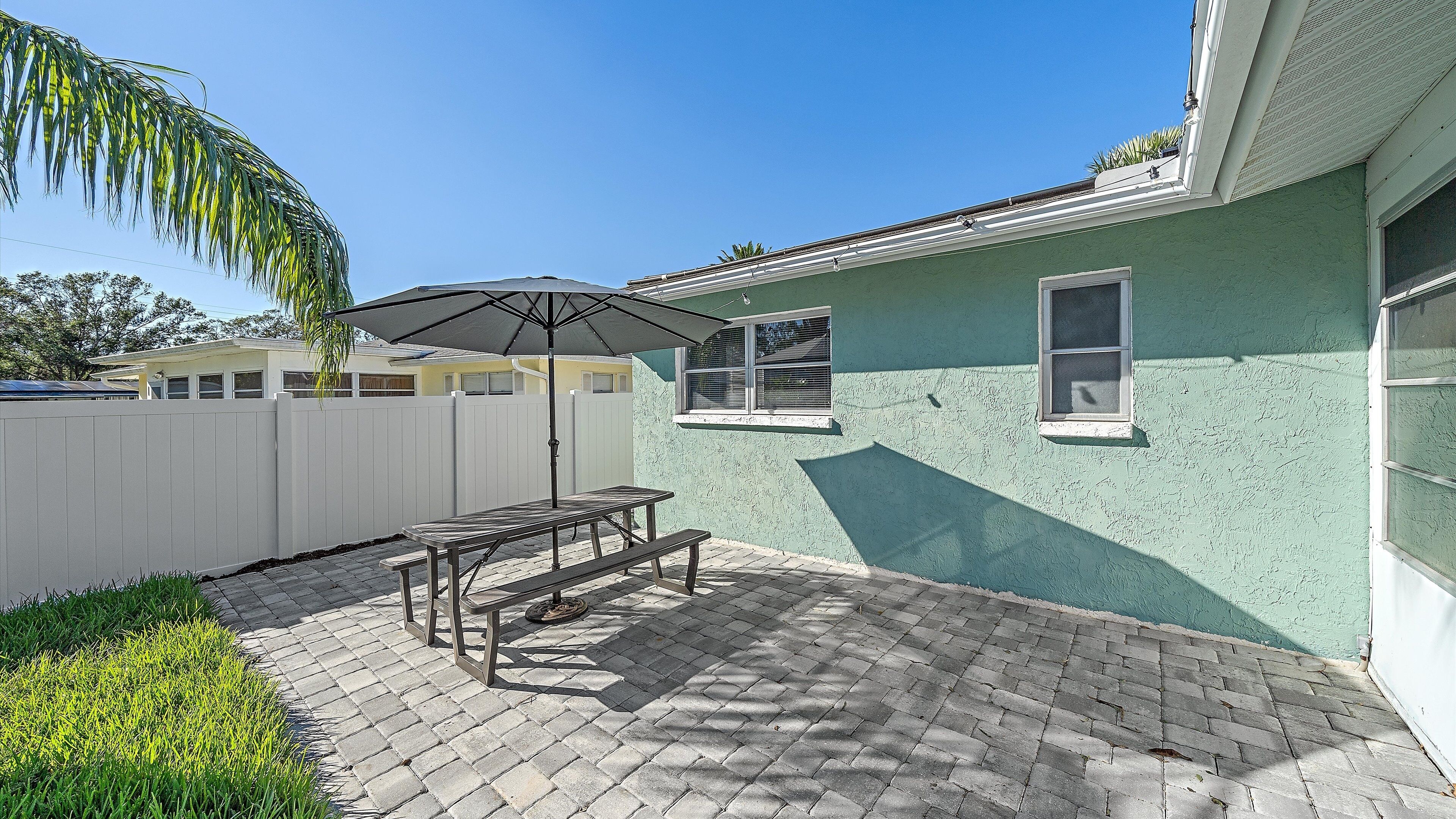 A patio with a table and umbrella, a white fence, and a house with a green exterior.