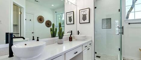 A modern bathroom with a large white sink, a glass shower enclosure, and decorative wall art.