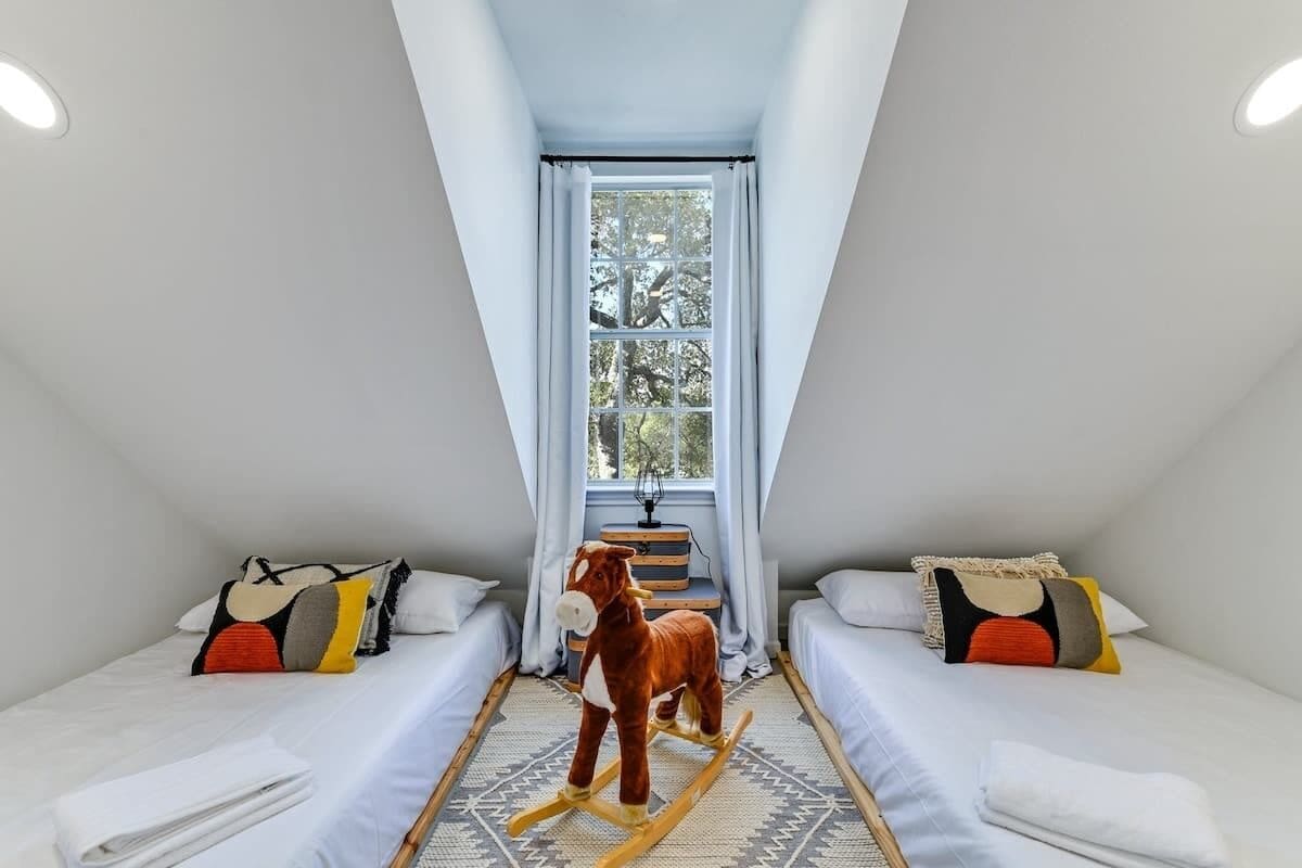 A small, triangular room with two beds, a rocking horse, and a window with curtains.