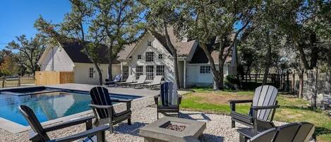 A backyard with a swimming pool, Adirondack chairs, and a fire pit.