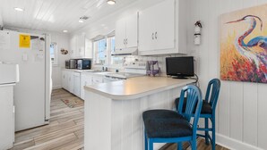 A modern kitchen with white cabinetry, a central island, and a large painting of a bird. - Inlet Front Beach House 4BR 4BA Pet Friendly Private Dock (Garden City Beach)